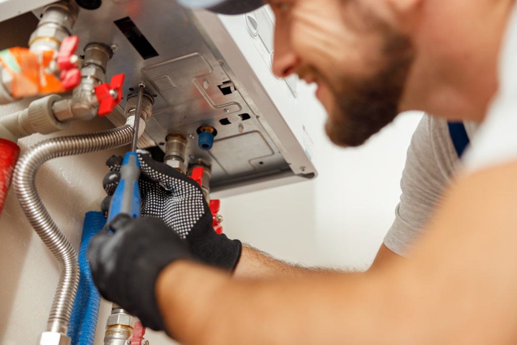 Closeup of plumber using screwdriver while installing new steel hot water central heating system in apartment