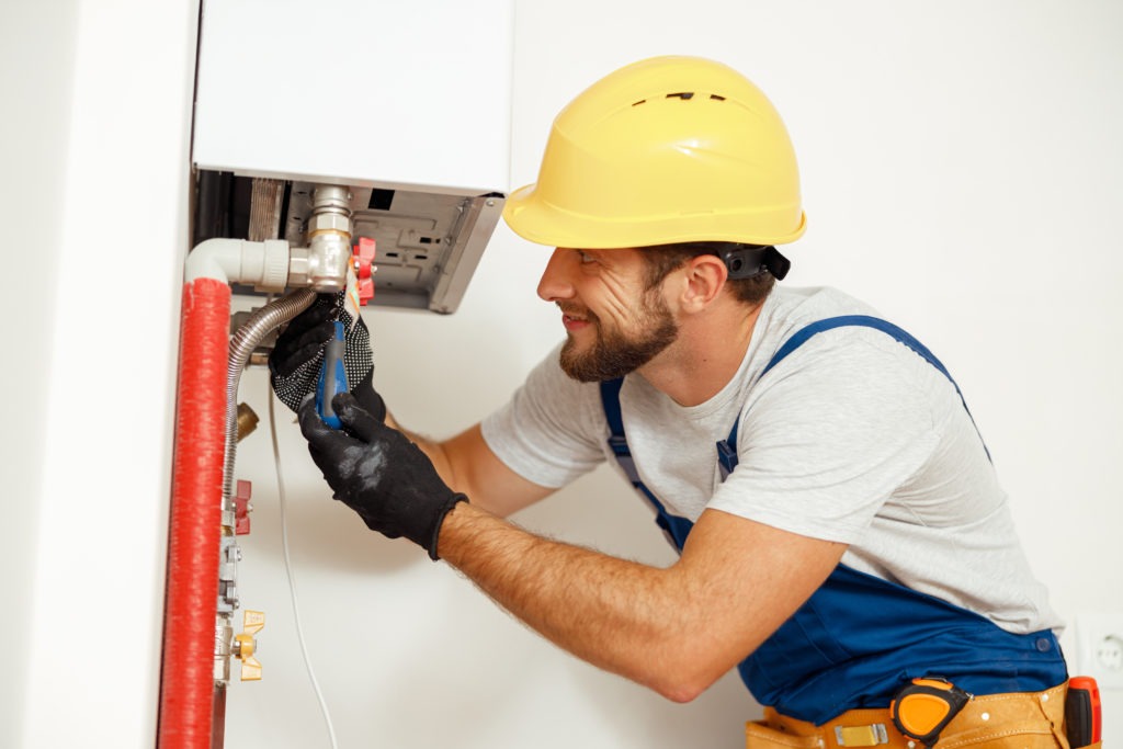Side view of handyman, technician using screwdriver while fixing boiler or water heater, working on heating system in apartment